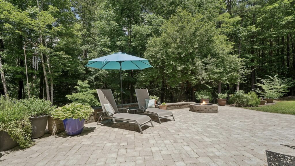 The deck leads down to a stunning stone patio with fire pit, perfect for entertaining or simply unwinding. The large, fenced yard with its meticulously maintained landscaping offers a peaceful retreat where you can relax and enjoy the outdoors.